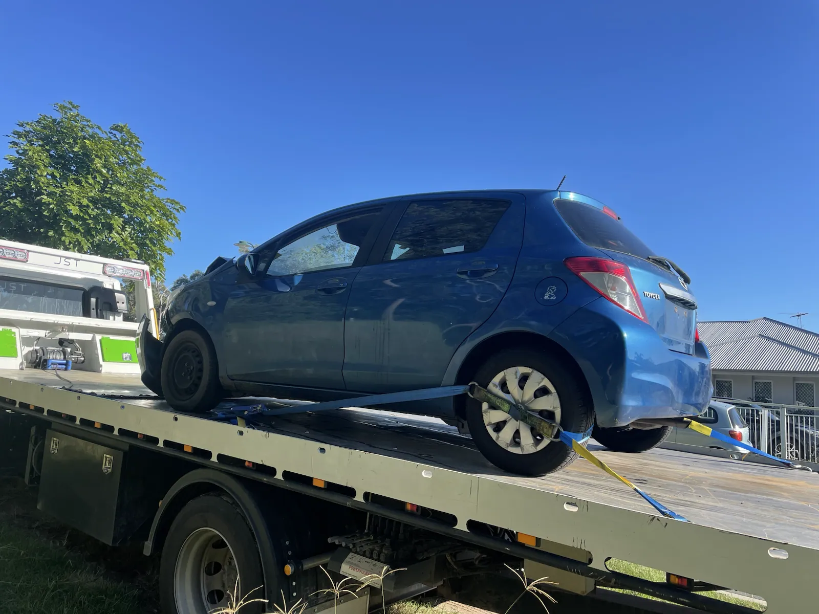 Blue hatchback loaded on a tow truck for removal