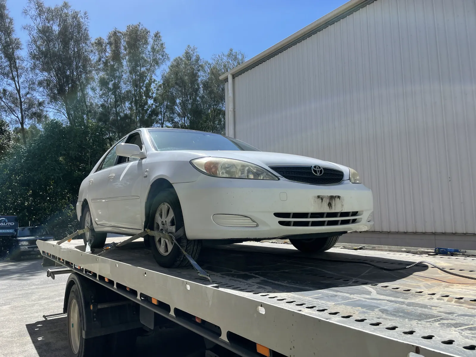 White sedan loaded on a tilt tray for cash for cars removal